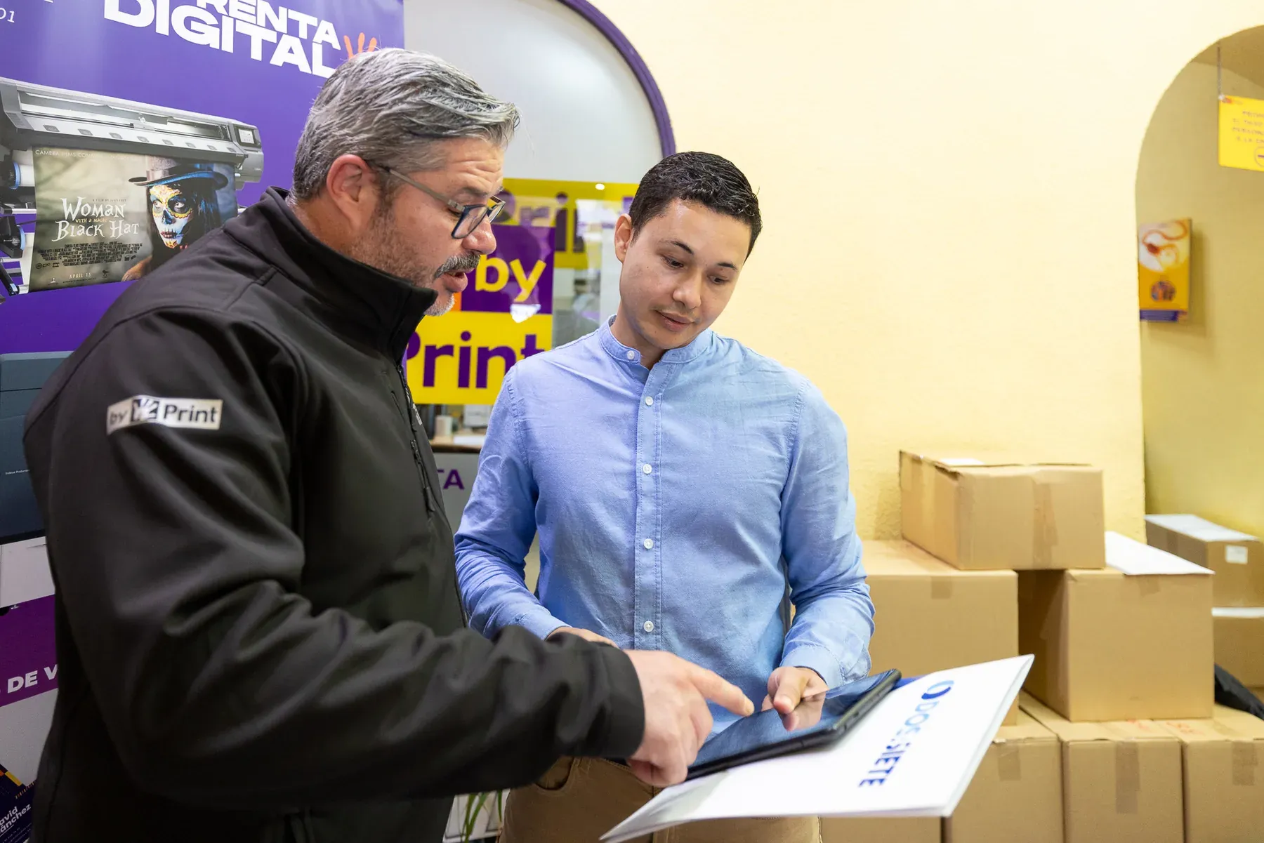 Dos profesionales revisan una tableta durante una visita a una imprenta. Fotografía original.