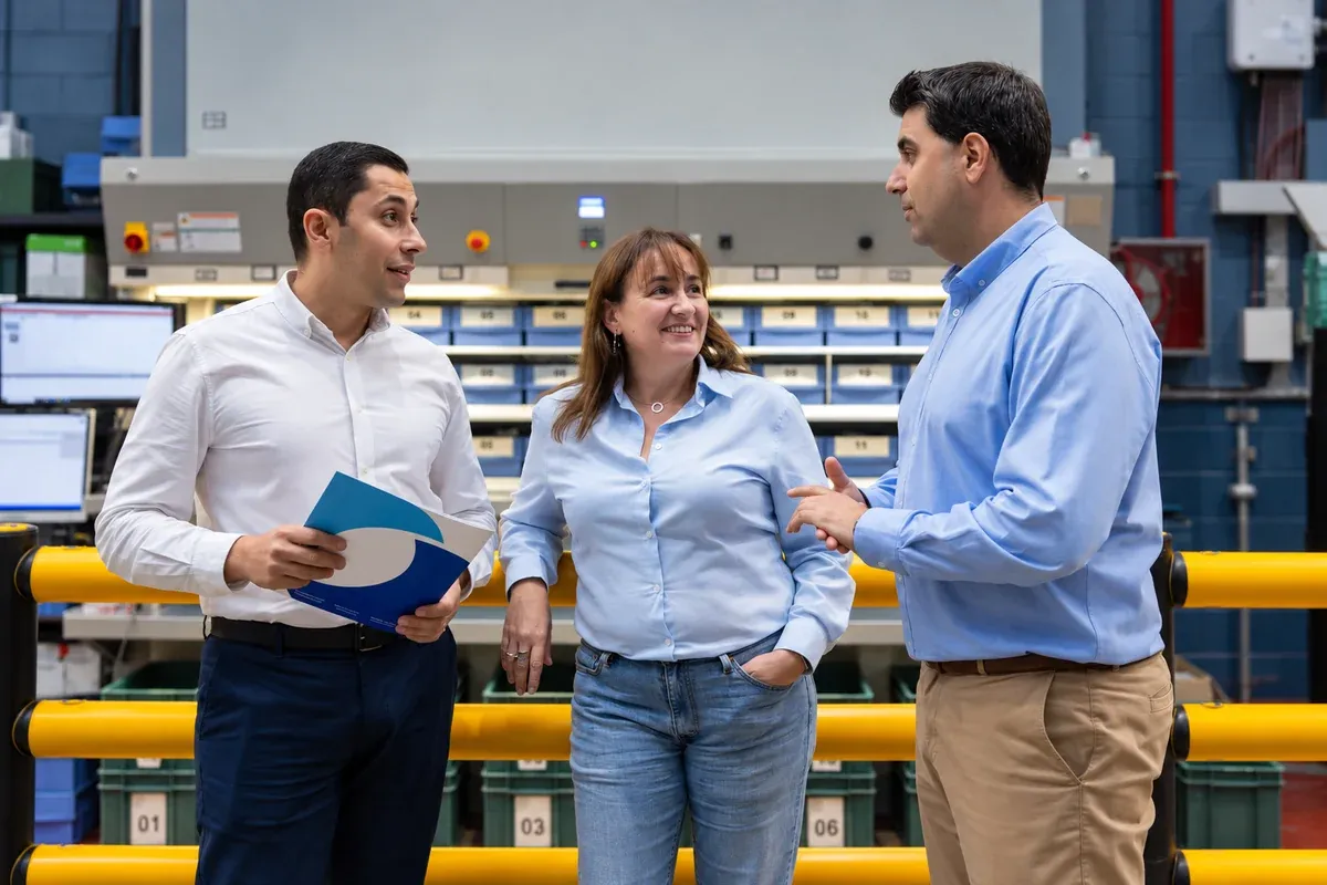Tres personas conversan durante una visita a un entorno industrial. Fotografía adaptada.